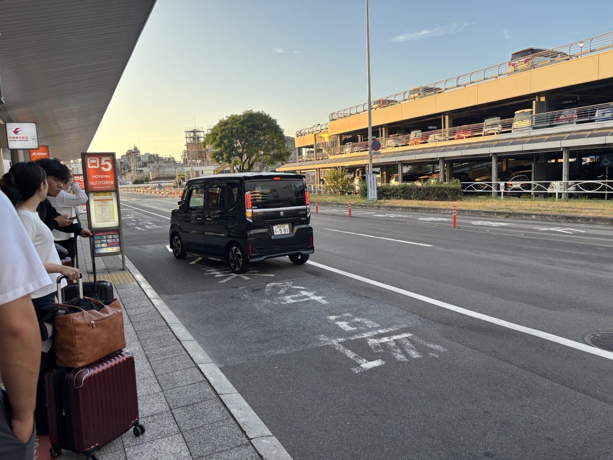 松山空港の伊予鉄バスのりば5番でスーツケースを持って待つ人たち